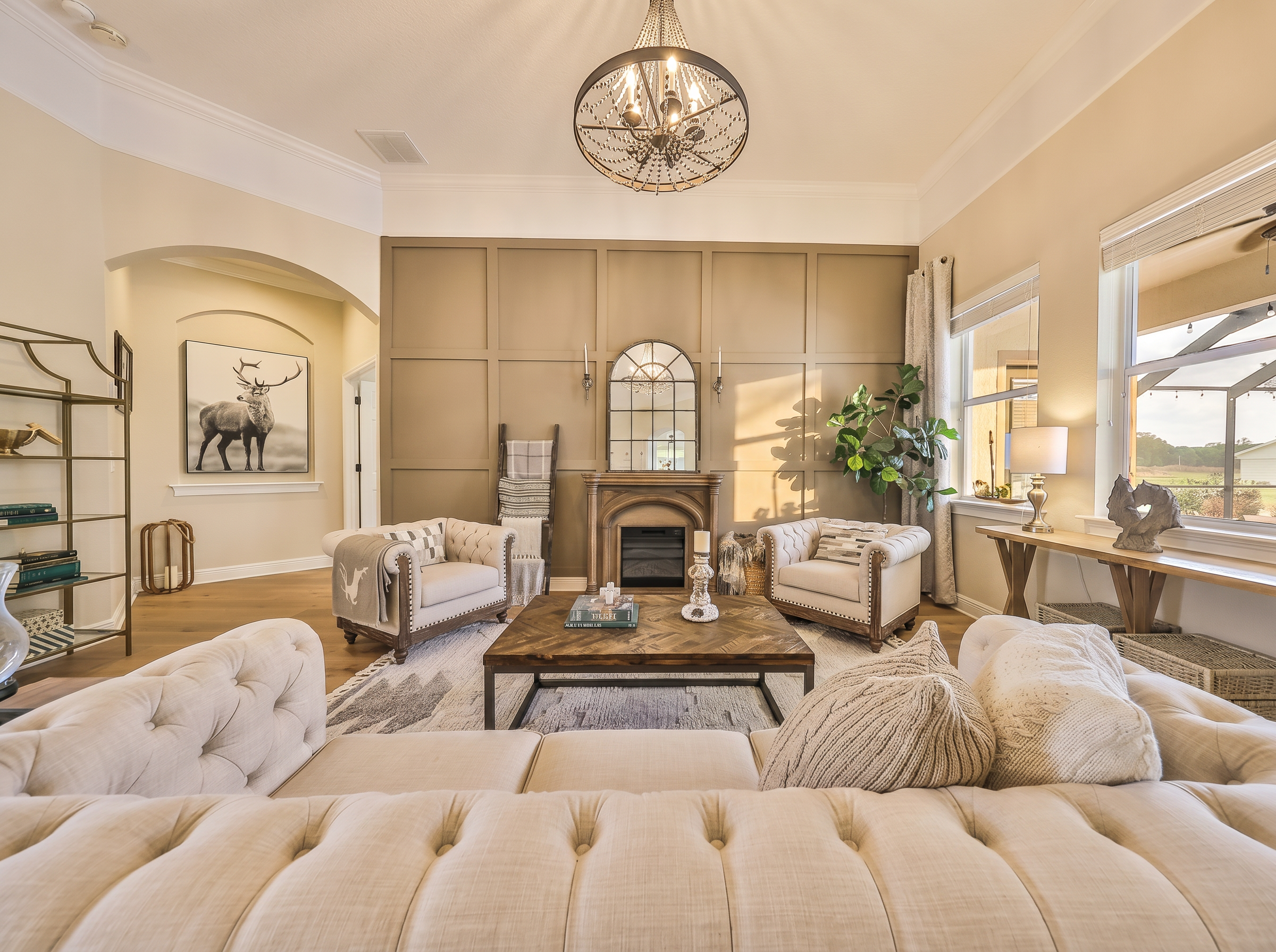 Formal living room with taupe board-and-batten accent wall, tufted Chesterfield sofas, beaded chandelier, and arched mirror over fireplace — Lithia, FL